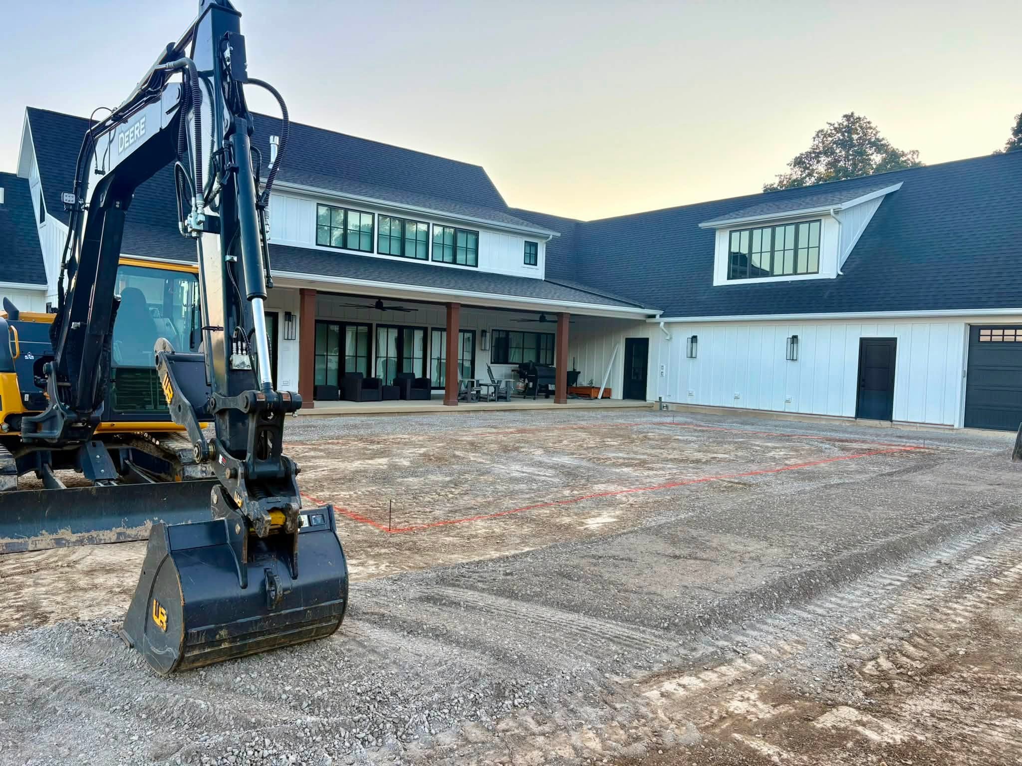 Excavator beside a marked gravel area in a backyard before inground pool excavation.