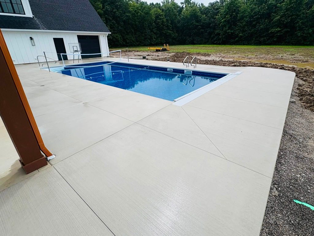 Rectangular inground pool with a concrete surround, volleyball net, and ladder beside a white building